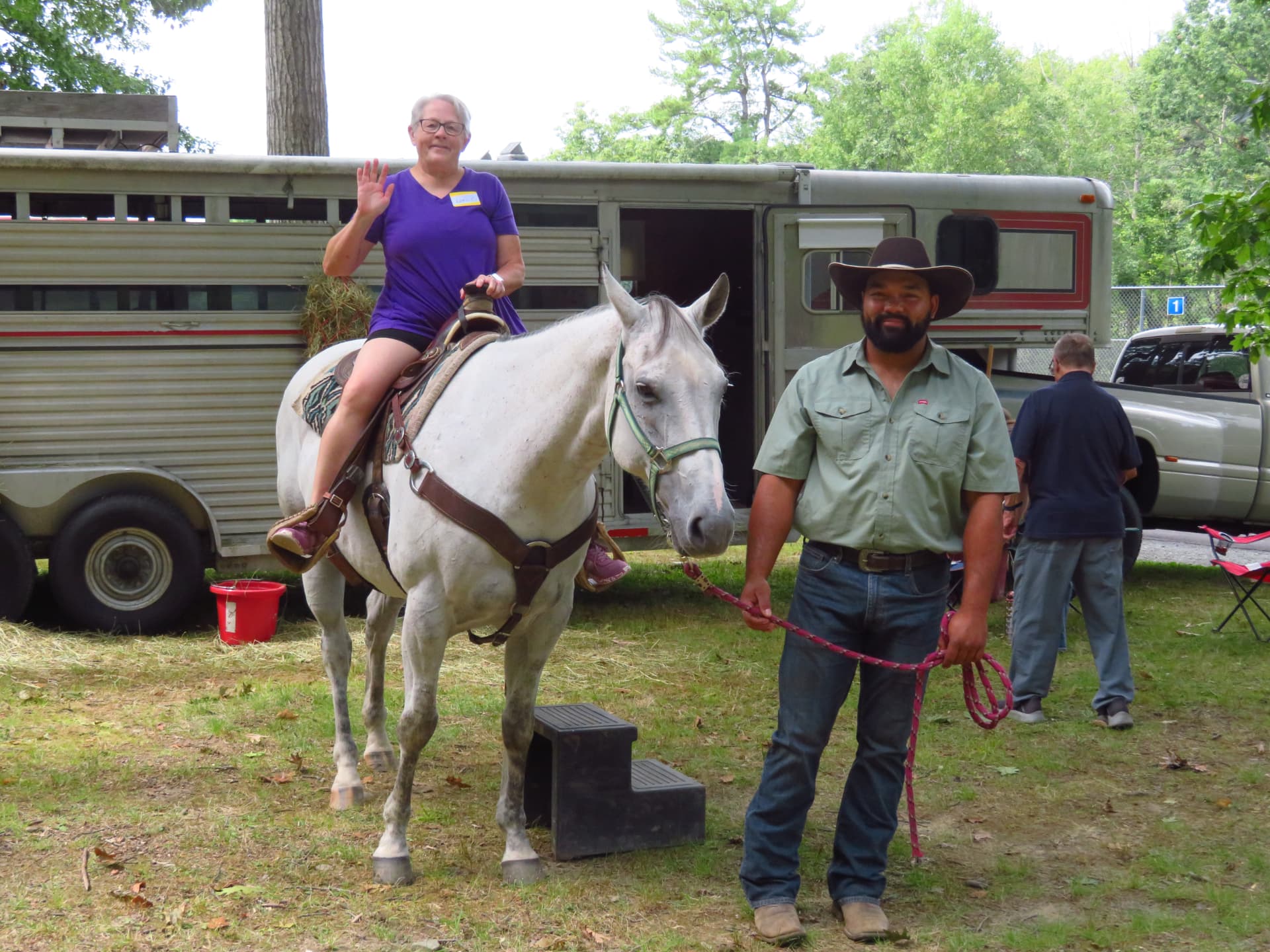 A member waving from horseback beside the horse trailer